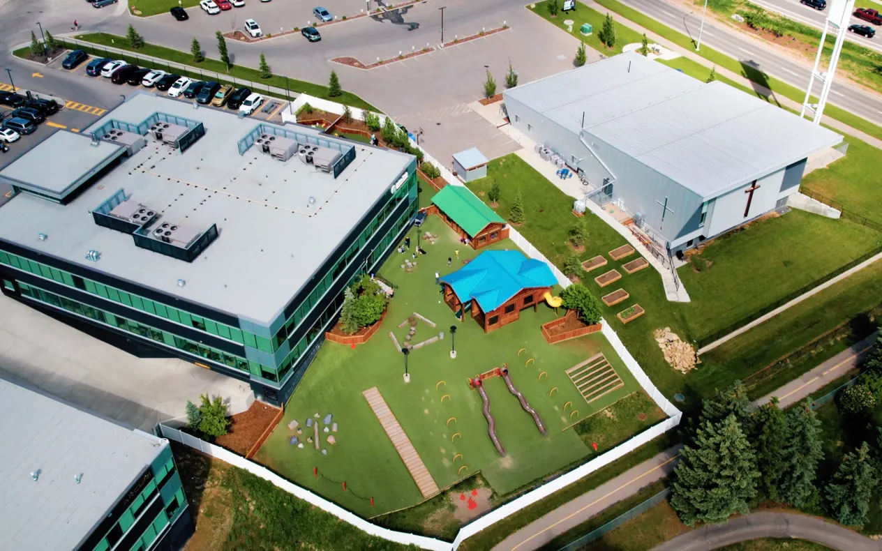 Aerial view of an Active Start Child Care center with live ChildFriendly Pro callouts over the bus lane, classrooms, playground and parent app