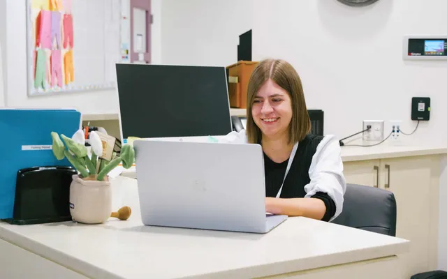 A smiling administrator working on a laptop at the front office desk