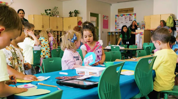 Children doing crafts at classroom tables while educators help in the background
