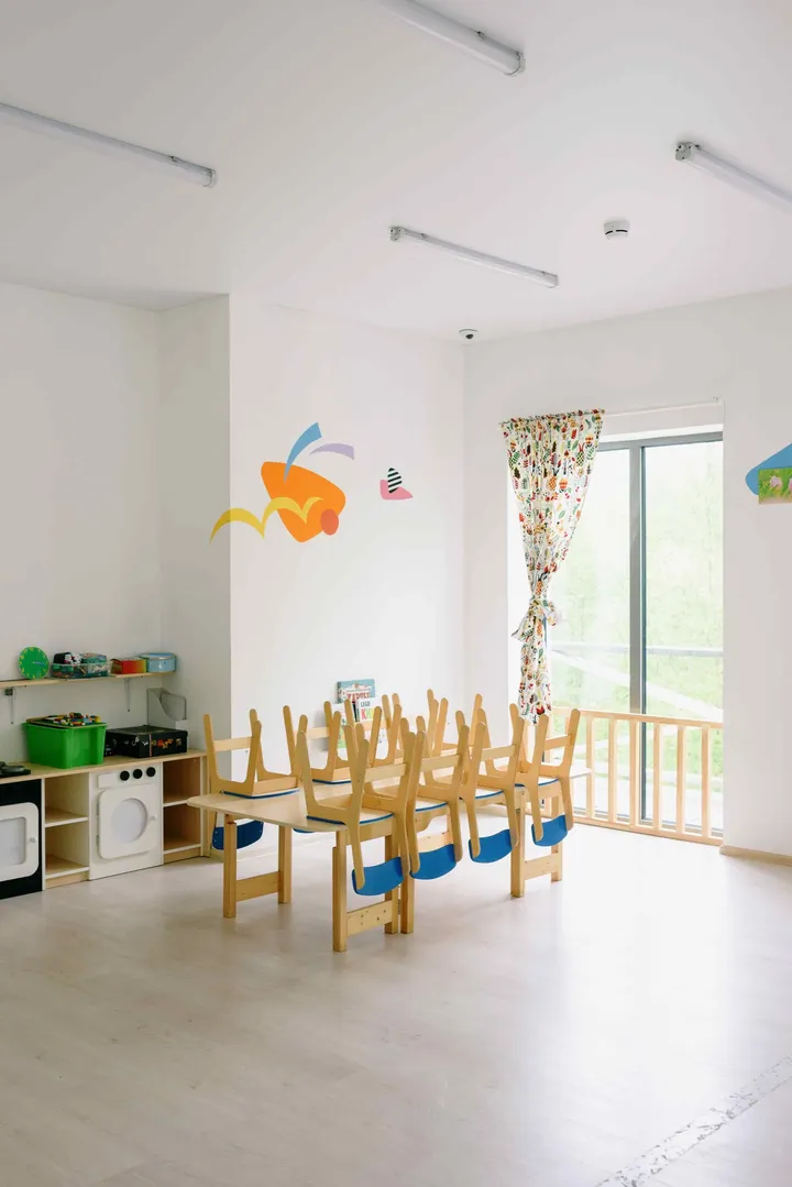 A daycare classroom with child-sized chairs and a play kitchen
