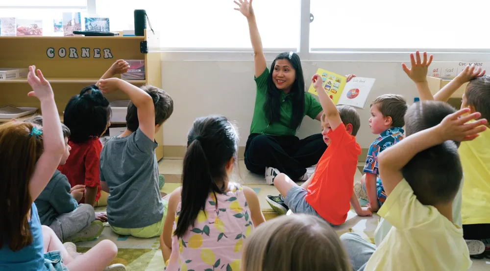 An educator leading circle time with children raising their hands