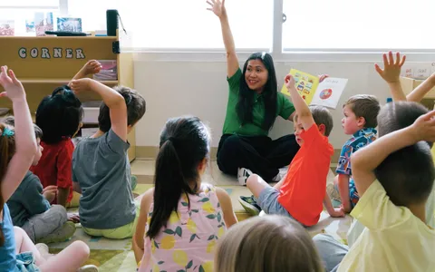 An educator leading circle time with children raising their hands