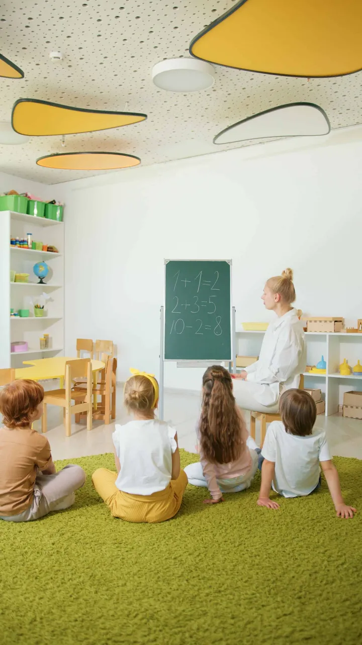 An educator teaching at a chalkboard while children sit for circle time