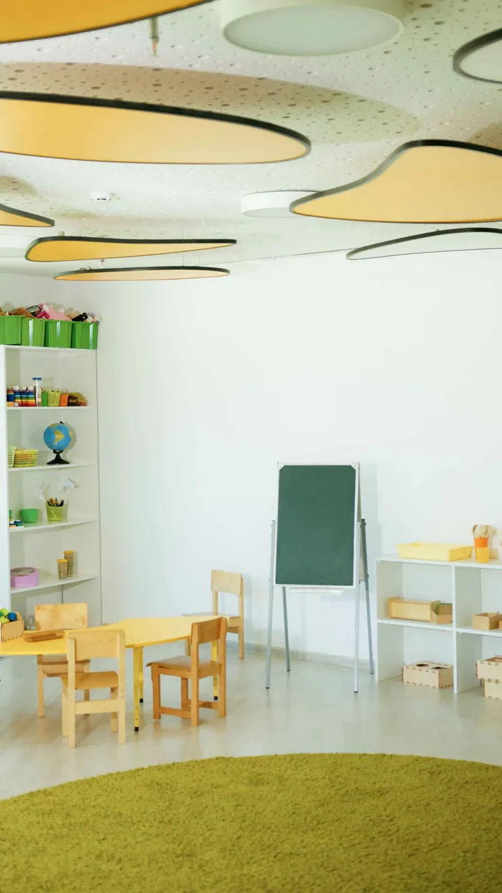 A tidy preschool classroom with a chalkboard easel, small tables and toy shelves
