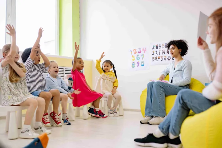Children raising their hands during a lesson in a bright classroom