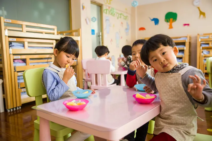 Preschoolers eating snack together at a pink table in a daycare room