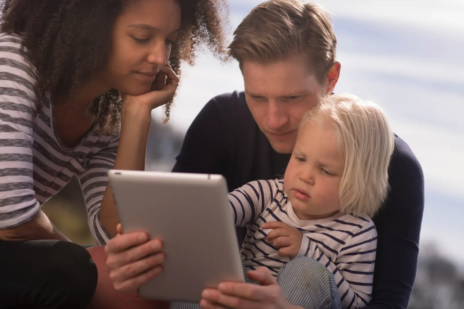 Parents reviewing child care updates on iPad with child.