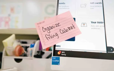 A pink to-do sticky note reading “Organize filing cabinet” stuck to an office monitor