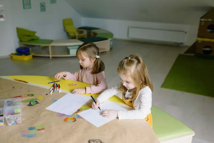 Two girls colouring side by side at a daycare table