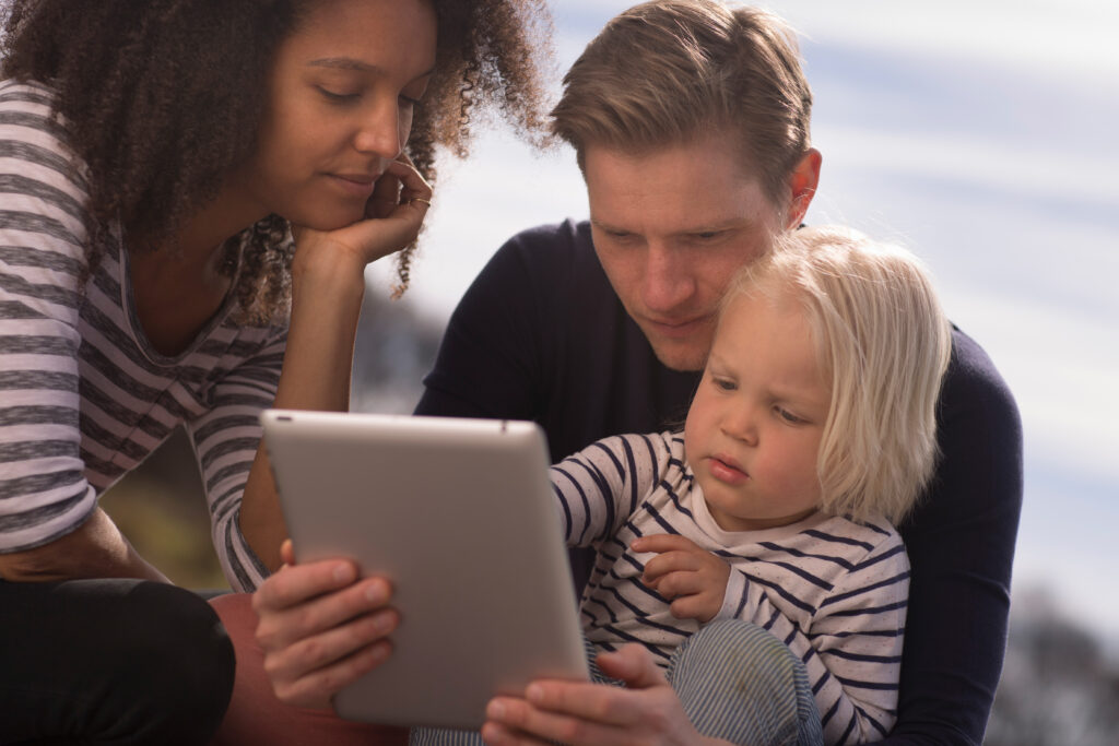 Parents reviewing childcare updates on iPad with child.